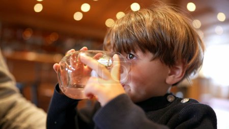 Photo for Little boy sipping water at restaurant. Child drinking and hydrating himself holding glass - Royalty Free Image
