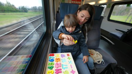 Foto de Mamá proactiva facilitando una actividad educativa para su hijo durante un viaje en tren rápido, ejemplificando el aprendizaje infantil en movimiento - Imagen libre de derechos