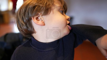 Téléchargez les photos : Idle Antics - Manchon mordant petit garçon, Expression de l'ennui en attendant au restaurant - en image libre de droit