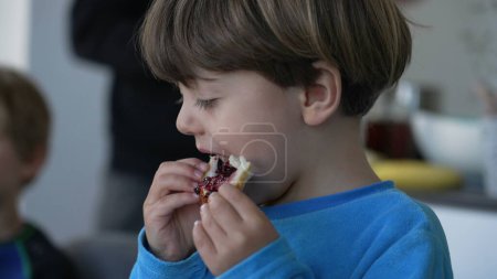 Foto de Niño comiendo pan brioche con gelatina para el desayuno. Primer plano de niño caucásico comiendo comida en la mañana, escena de estilo de vida franca - Imagen libre de derechos