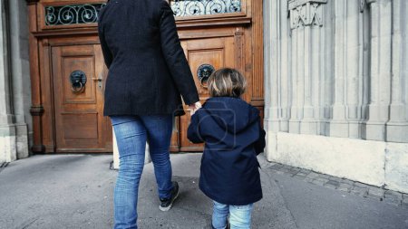 Téléchargez les photos : Mère et enfant tenant la main marchant dans le temple religieux atteignant la poignée de porte et s'ouvrant à la porte traditionnelle en bois - en image libre de droit
