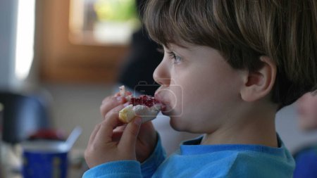 Foto de Pequeño chico caucásico disfrutando de Brioche con jalea en el desayuno, comida de carbohidratos para niños - Imagen libre de derechos