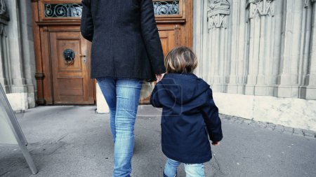 Photo for Mother and child holding hands walking into Religious temple reaching for doorknob and opening to wooden traditional door - Royalty Free Image
