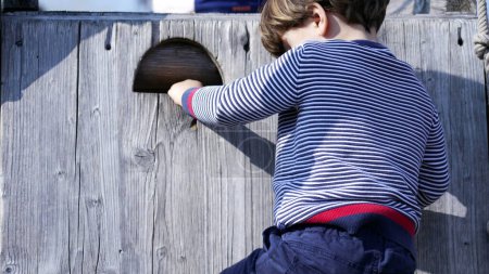 Téléchargez les photos : Petit garçon escalade structure de terrain de jeu maintenant l'équilibre. Enfant montant sur une échelle en bois - en image libre de droit