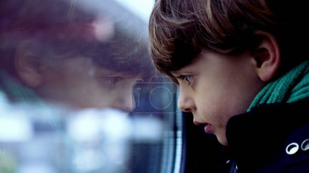 Téléchargez les photos : Enfant pensif penché sur la fenêtre du train avec une expression réfléchie, profil gros plan visage de l'enfant observant le monde - en image libre de droit