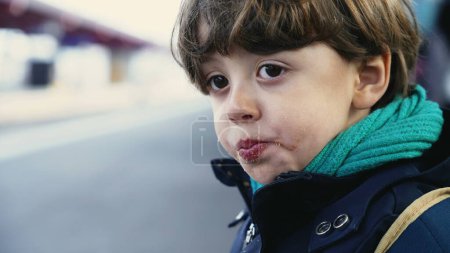 Photo for Portrait of young boy waiting for train standing at platform wearing scarf and jacket during autumn fall season, close-up face of 4 year old child chewing food - Royalty Free Image
