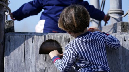 Foto de Niño pequeño escalando la estructura del patio de recreo manteniendo el equilibrio. Niño subiendo en escalera de madera - Imagen libre de derechos