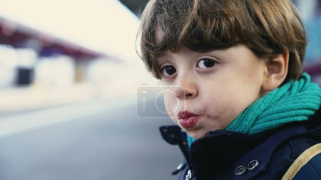 Photo for Portrait of young boy waiting for train standing at platform wearing scarf and jacket during autumn fall season, close-up face of 4 year old child chewing food - Royalty Free Image