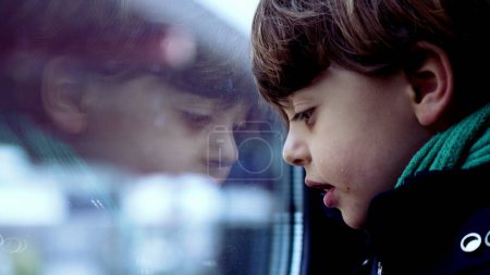 Foto de Niño pensativo apoyado en la ventana del tren con expresión reflexiva, perfil de primer plano cara de niño observando el mundo - Imagen libre de derechos