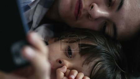 Foto de Primer plano íntimo de la madre y el niño, absorbido en la visualización de contenido en el teléfono celular mientras está acostado en la cama - Imagen libre de derechos