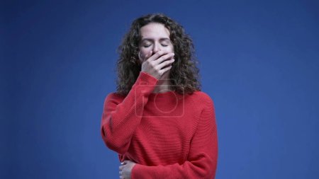 Téléchargez les photos : Femme fatiguée bâillant couvrant la bouche avec sensation de fatigue et d'ennui debout sur fond bleu - en image libre de droit