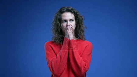 Téléchargez les photos : Femme pensive aux prises avec un dilemme debout sur fond bleu avec un pull rouge. Pensée 20s personne pendant la prise de décision difficile - en image libre de droit