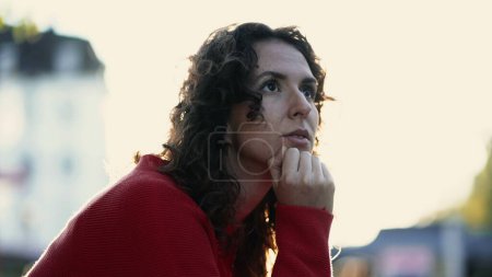 Téléchargez les photos : Femme réfléchie regardant à distance au coucher du soleil de la ville, visage rapproché d'une personne de 20 ans avec la main dans le menton dans la prise de décision introspective profonde, réfléchissant à la vie - en image libre de droit