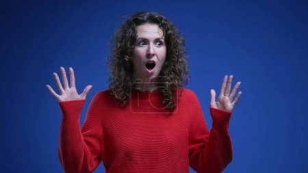 Foto de Joven mujer feliz reaccionando con Sorpresa y SHOCK acerca de fantásticas GRANDES noticias. 20s persona femenina se siente encantado por el logro en el telón de fondo azul - Imagen libre de derechos