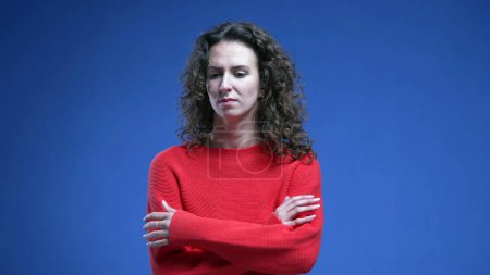 Photo for Upset woman crossing arms in frustration standing on blue background. thoughtful 20s female person in distraught dilemma - Royalty Free Image
