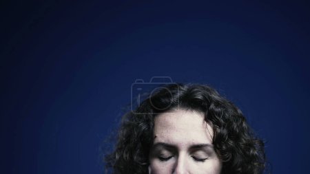 Foto de Mujer joven cerrando los ojos en meditación y relajación sobre fondo azul, frente de persona con espacio superior de la pantalla disponible para la animación - Imagen libre de derechos