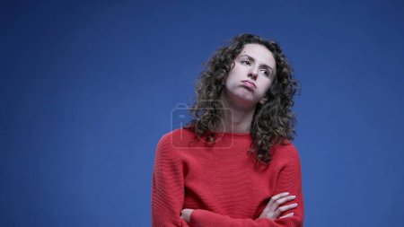 Photo for Woman feeling bored sighing deeply with arms crossed looking up and rolling eyes in boredom standing on blue backdrop - Royalty Free Image