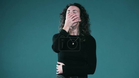 Téléchargez les photos : La personne épuisée couvre le bâillement de la bouche montrant le signal de fatigue debout sur le fond sarcelle - en image libre de droit
