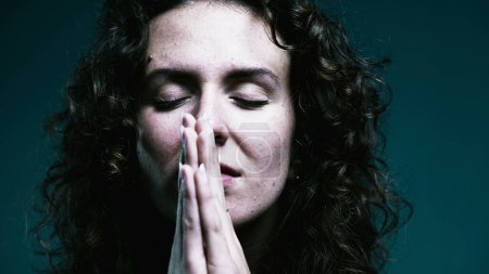 Faithful woman opening eyes to sky in PRAYER. Close-up face 20s person having HOPE during difficult times