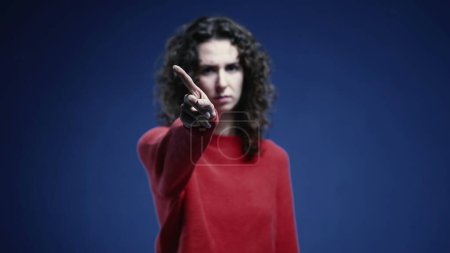 Photo for Young Woman Firmly Saying NO to Camera, 20s Woman Rejecting with Crossed Arms and Finger Wave, standing on blue backdrop - Royalty Free Image