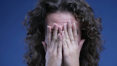 Foto de Mujer joven frustrada cubriendo la cara con las manos sintiendo pesar y ansiedad, cara de cerca de la persona femenina en los años 20 teniendo vergüenza de los recuerdos pasados - Imagen libre de derechos
