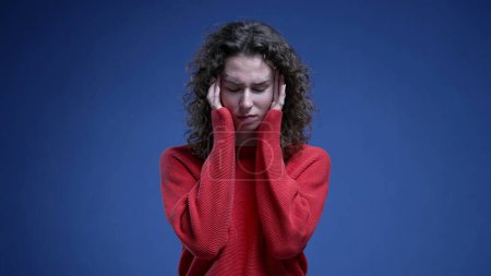 Téléchargez les photos : Jeune femme anxieuse avec des tempes de tête avec des mains luttant contre l'anxiété mentale se sentant submergé par des problèmes debout sur fond bleu - en image libre de droit