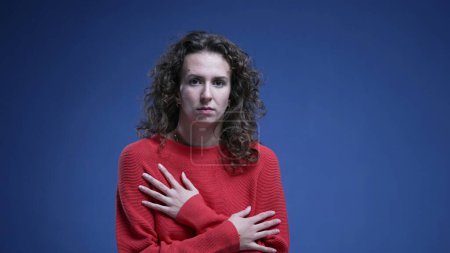 Photo for Scared young woman embracing herself hesitating showing fear and panicking on blue backdrop wearing red sweater. 20s female person afraid - Royalty Free Image