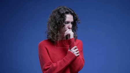 Photo for Anxious young woman biting nail in fear and nervousness. 20s female person feeling scared and fearful standing on blue backdrop - Royalty Free Image
