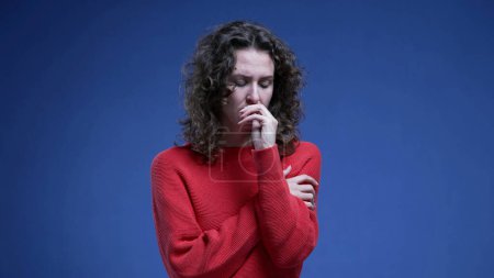 Foto de Mujer joven y ansiosa mordiendo uñas con miedo y nerviosismo. 20s persona femenina sensación de miedo y miedo de pie sobre fondo azul - Imagen libre de derechos