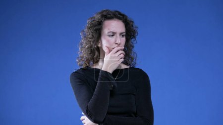 Photo for Pensive woman thinking deeply with hand in chin pondering solution to problem. Thoughful preoccupied person on blue background - Royalty Free Image