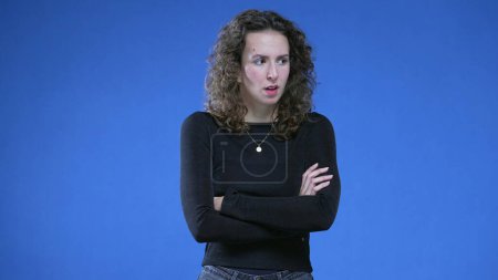 Photo for Upset woman crossing arms looking at camera while standing on blue background. Angry female 20s person not liking offer, gesturing disapproval with body language - Royalty Free Image