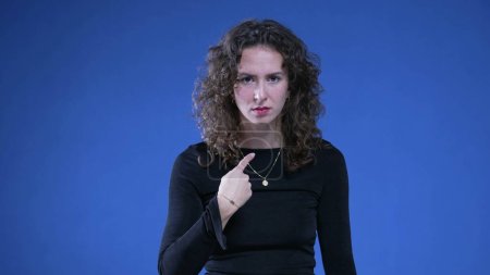 Photo for Woman pointing at herself in confusion with finger in disbelief and consternation standing on blue background. 20s person reacting to accusation - Royalty Free Image