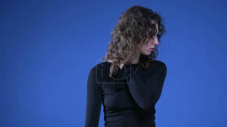 Photo for Stressed young woman rubbing neck trying to appease mental anguish while standing on blue background - Royalty Free Image