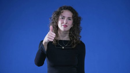 Photo for Happy woman showing approval with thumb up, looking at camera while standing on blue background. Approved concept - Royalty Free Image