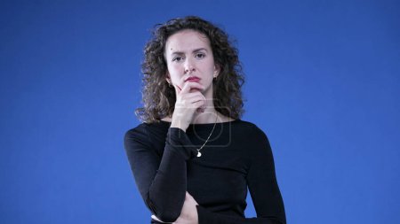 Photo for Pensive woman thinking deeply with hand in chin pondering solution to problem. Thoughful preoccupied person on blue background - Royalty Free Image