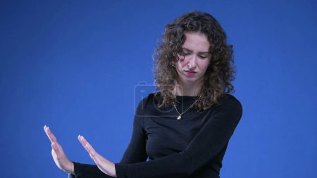 Foto de 20s Mujer expresando rechazo y disgusto con gesto de mano, mujer empujando con las manos hacia los lados sobre fondo azul - Imagen libre de derechos