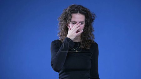 Photo for Anxious woman in panic mode pulling hair and fidgetting body language standing on blue background. Desperate person feeling preoccupied during difficult times - Royalty Free Image
