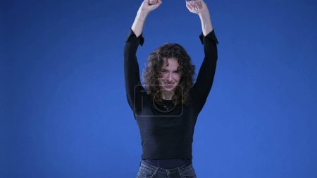 Foto de Mujer feliz celebrando el éxito levantando puños en el aire mirando a la cámara mientras está de pie sobre fondo azul - Imagen libre de derechos