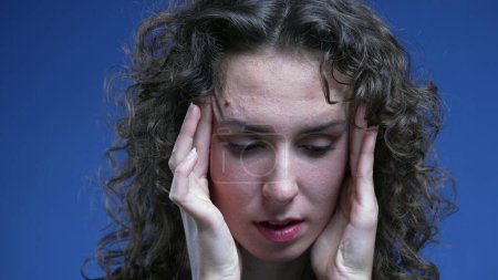 Foto de Mujer joven abrumada estresada tratando de calmar su nerviosismo poniendo las manos en el lado de las sienes de la cabeza sintiendo frustración y ansiedad - Imagen libre de derechos