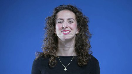 Photo for Portrait of a young woman smiling at camera on blue background. 20s female caucasian person with curly hair - Royalty Free Image