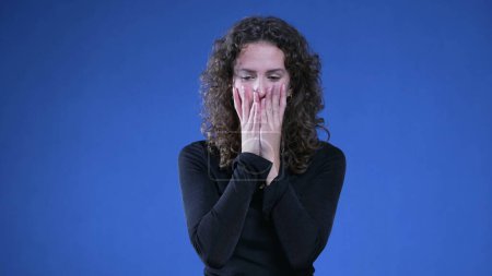 Photo for Anxious woman in panic mode pulling hair and fidgetting body language standing on blue background. Desperate person feeling preoccupied during difficult times - Royalty Free Image