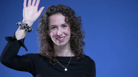 Photo for Woman waving hello with hand, happy person saying HI with positive emotion standing on blue background - Royalty Free Image
