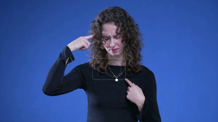 Photo for Young Woman in Shock Pointing to Herself Over Accusation signalling that accuser is crazy or wacky standing on blue background, pointing finger at herself in disbelief - Royalty Free Image
