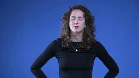 Photo for Annoyed woman rolling eyes in disgust and contempt while standing on blue background with hands on hips - Royalty Free Image