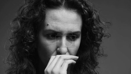 Photo for Preoccupied young woman biting nails feeling overwhelmed with problems. person struggling with crippling anxiety captured in intense dramatic monochromatic black and white - Royalty Free Image