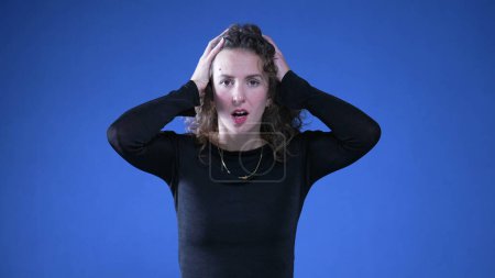 Photo for Shocked woman putting hands on top of head staring at camera in disbelief and surprise by unexpected news standing on blue background - Royalty Free Image