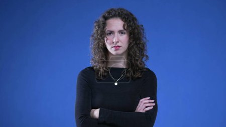 Photo for Upset woman with arms crossed looking at camera with angry expression, standing on blue background. Female person in 20s with negative body language - Royalty Free Image