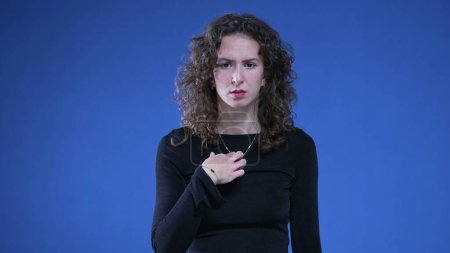 Photo for Woman pointing at herself in confusion with finger in disbelief and consternation standing on blue background. 20s person reacting to accusation - Royalty Free Image