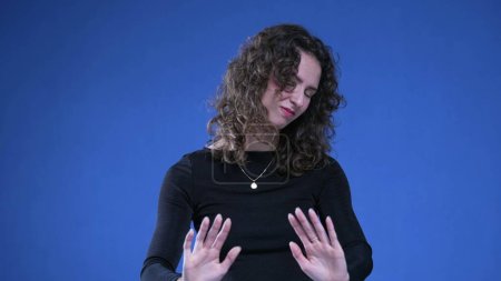 Photo for Woman pushing away with hands looking at camera. Female person in 20s signalling refusal and disgust standing on blue background - Royalty Free Image