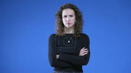 Photo for Upset woman crossing arms looking at camera while standing on blue background. Angry female 20s person not liking offer, gesturing disapproval with body language - Royalty Free Image